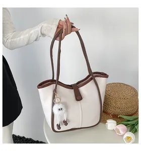 Detail of cream tote bag with brown trim and cute plush monster pendant accessory