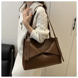 Brown leather tote bag showing a symmetric folded design and adjustable strap on a model