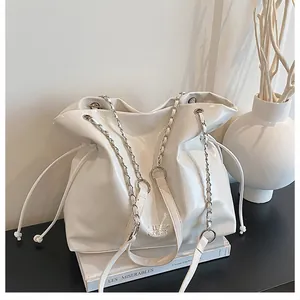 Sac seau en cuir verni blanc avec chaîne argentée posé sur un livre de décor