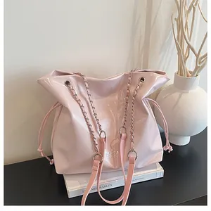 Détail d'un grand sac cabas rose pâle en cuir verni avec chaîne argentée sur un livre