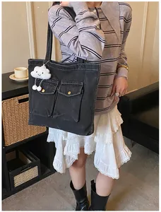 Detail of black canvas tote bag with flap pockets and cute cloud plush charm accessory