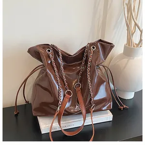 Détail d'un cabas marron brillant avec poignée en chaîne et bandoulière en cuir