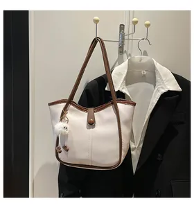 Detail of white tote bag with brown leather trim and cute fuzzy eye charm on suit