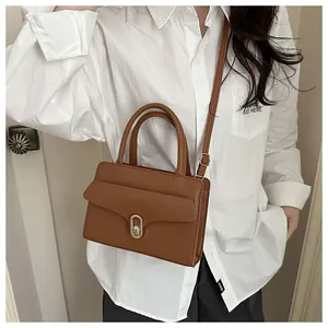 Detail showing the brown lychee leather texture and golden metal twist lock of the handbag