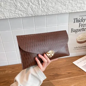 Dunkelbraune Umschlagtasche mit Epi-Textur und goldener Schnalle in der Hand