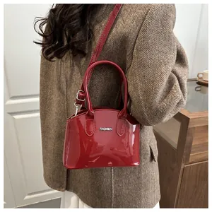 Detail of red patent leather handbag with metallic Fashion logo and adjustable shoulder strap