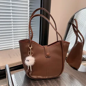 Elegant brown leather tote bag with long handles and a cute plush charm accessory