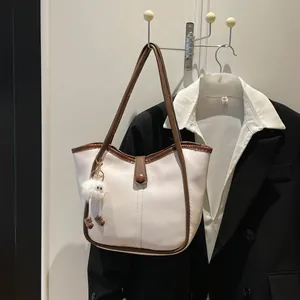 Chic white canvas tote bag with brown leather trim and cute plush charm on a suit hanger