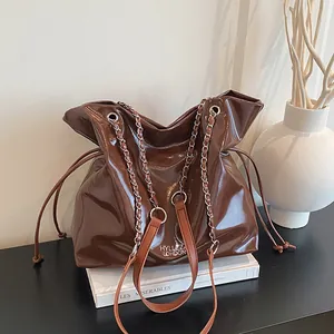 Borsa tote marrone scuro lucida con manici a catena e tracolla mostrata in natura morta