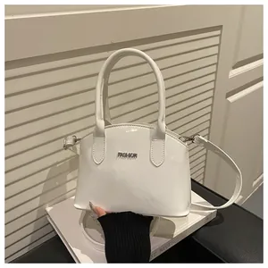 Detail of white patent leather handbag featuring silver metal FASHION lettering and strap