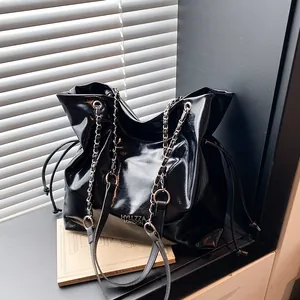 Borsa tote nera lucida con tracolla a catena in metallo su un davanzale soleggiato