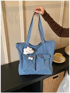 Detail of blue denim tote bag with dual front pockets and white cloud plush charm