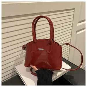 Detail of burgundy glossy patent leather handbag with dual handles and metal FASHION logo