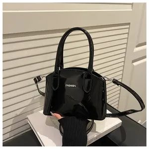 Detail of glossy black patent leather shell bag with silver FASHION metal logo