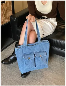 Detail of blue denim tote bag with two front pockets and bronze metal buttons on sofa