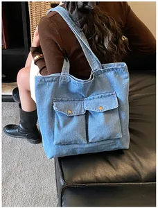 Close-up of light blue denim tote bag featuring dual front pockets with gold metal buttons