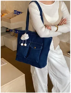 Detail of blue denim tote bag with front pockets and white cloud plush charm accessory