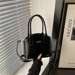Fashionable black glossy patent leather handbag with silver lettering and shoulder strap