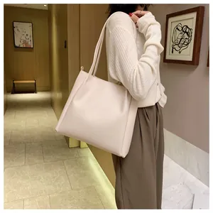 Lifestyle shot of model wearing a large beige tote bag in a modern indoor corridor