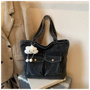 Detail of dark grey washed denim tote bag with large front pockets and cloud charm pendant
