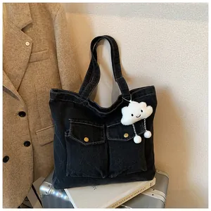 Detail of black denim tote bag featuring dual flap pockets and a plush cloud charm accessory