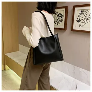 Detail of a large black matte leather tote bag worn as a shoulder bag by a model