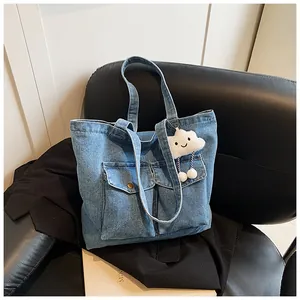 Detail of blue denim tote bag featuring dual front pockets and a white cloud plush charm