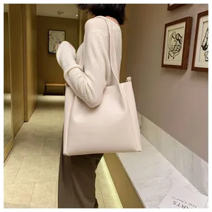 Minimalist beige tote bag shown on shoulder in a modern indoor setting