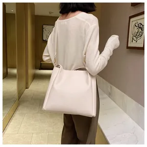 Minimalist beige oversized tote bag shown on shoulder in a modern indoor setting