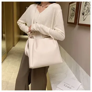 Detail of a large off-white tote bag in matte faux leather worn with a beige sweater