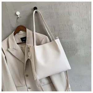 Detail of minimalist cream tote bag with adjustable strap against a grey wall