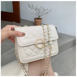Close-up of pearl buckle and metal chain strap on beige quilted crossbody bag