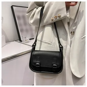 Detail of a minimalist black flap bag with vertical buckle straps on a white blazer