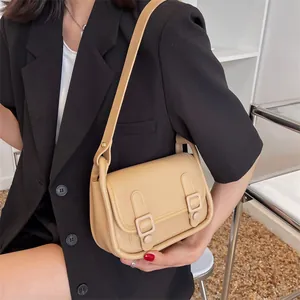 Beige faux leather crossbody bag with flap and decorative straps on black blazer