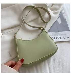 Close-up of light green moon-shaped leather bag with golden hardware on white fabric