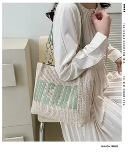 Close-up of woven straw tote bag featuring green Micada lettering and chain strap detail