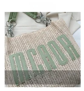 Detail of woven straw tote featuring green leather letters and metal chain strap