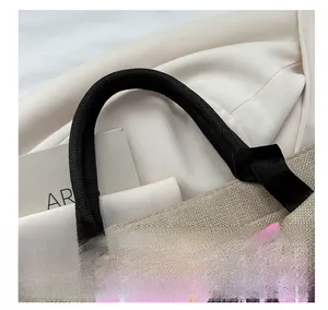 Detail of hand-woven black rope handle on a textured straw tote bag with palm prints