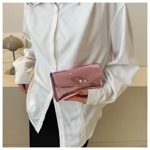 Detail view of a pink metallic envelope clutch bag held by a model in a warm setting