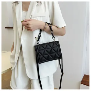 Detail of black geometric quilted crossbody bag with thick acrylic chain on a white suit