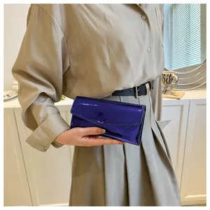 Close-up of vibrant royal blue patent leather envelope clutch bag held by a model