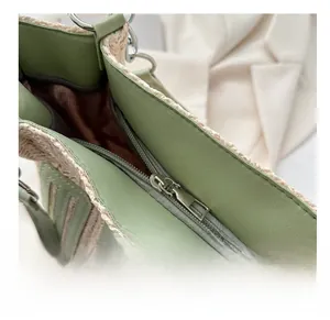 Close-up of the smooth zipper and green leather stitching on the straw tote bag