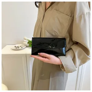 Glossy black patent leather envelope clutch bag held in a cozy home lifestyle setting