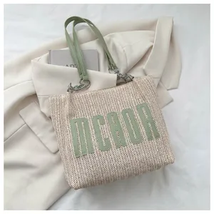 Detail of woven straw tote bag with green leather straps and letter patch on a blazer