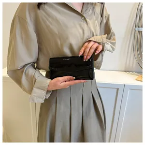 Close-up of black patent leather envelope clutch bag held by a model in a minimalist setting