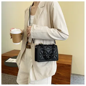 Close-up of black quilted shoulder bag featuring chunky acrylic chain and sleek flap closure