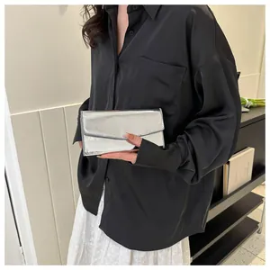Close-up of a silver mirror finish envelope clutch bag held by a model in a modern room