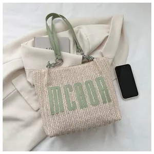 Top view of a woven straw tote bag with green leather straps and MCAOR logo lettering