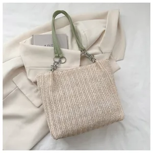 Close-up of woven straw tote bag with green leather handles and silver metal chain detail