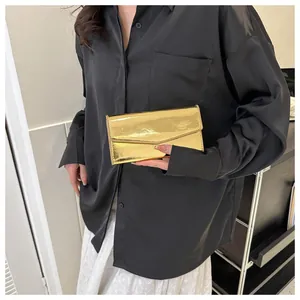 Close-up of a glossy gold envelope clutch bag held by a model in a black shirt